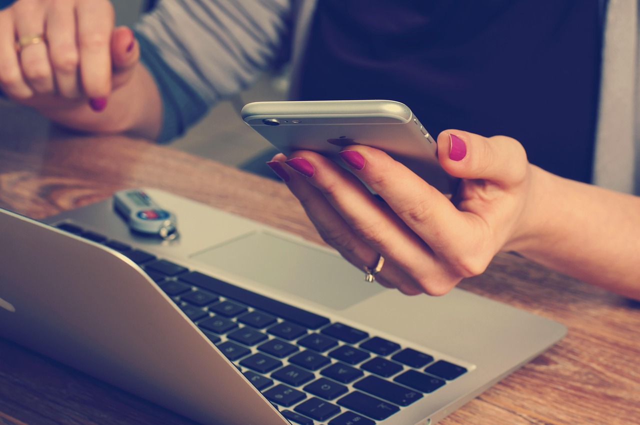 Mâini care țin un telefon deasupra unui laptop